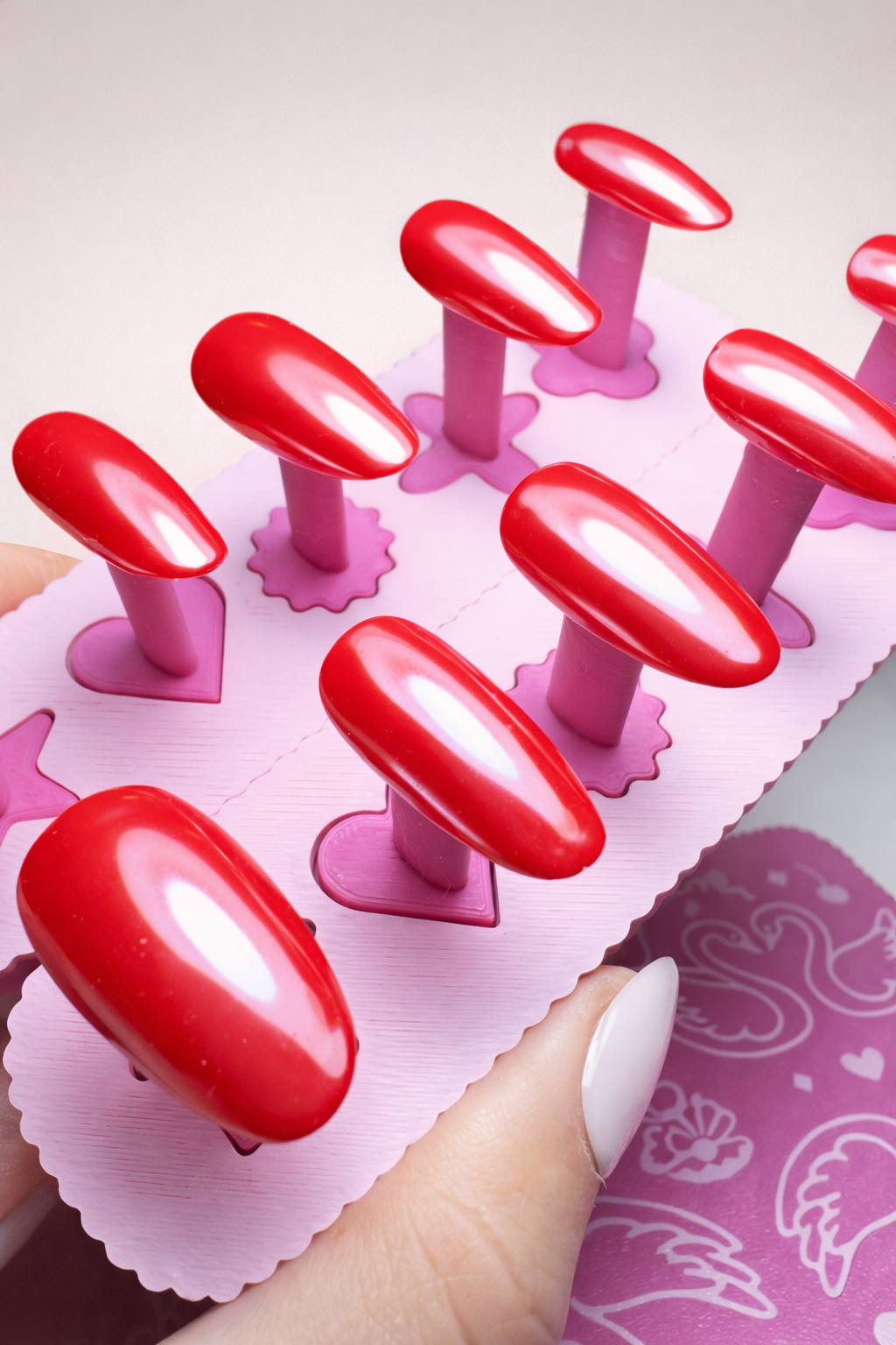 Set of 10 scarlet press on nails with chrome highlights and glossy top coat. Almond shape on a pink nail stand.